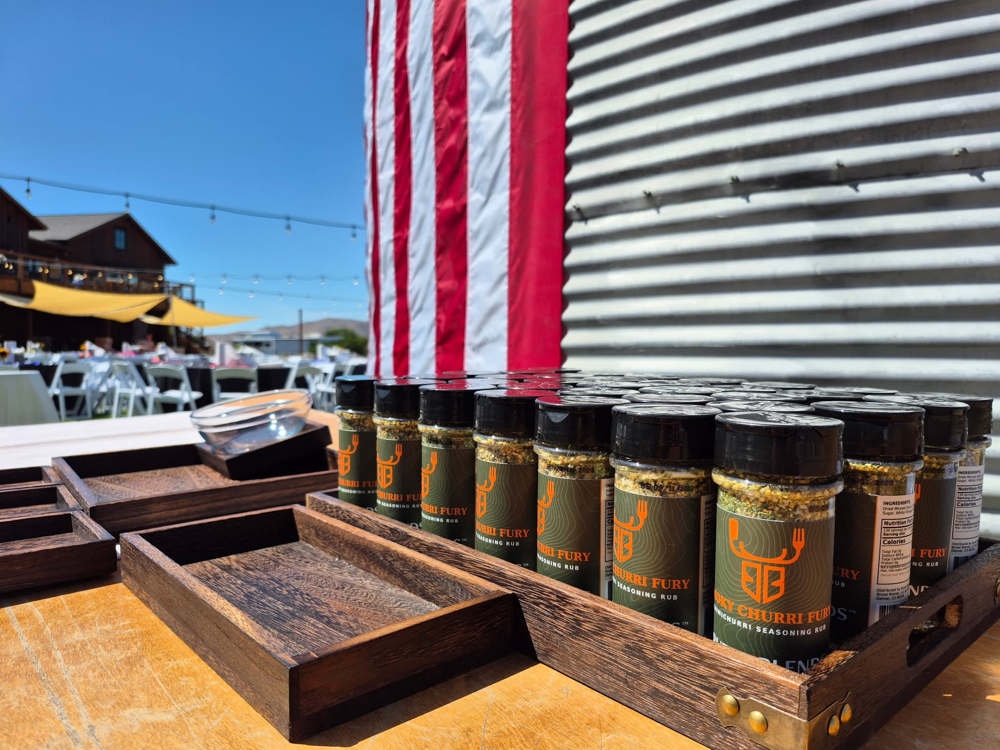 Churri Fury seasoning rub jars in wooden trays outdoors with an American flag backdrop.